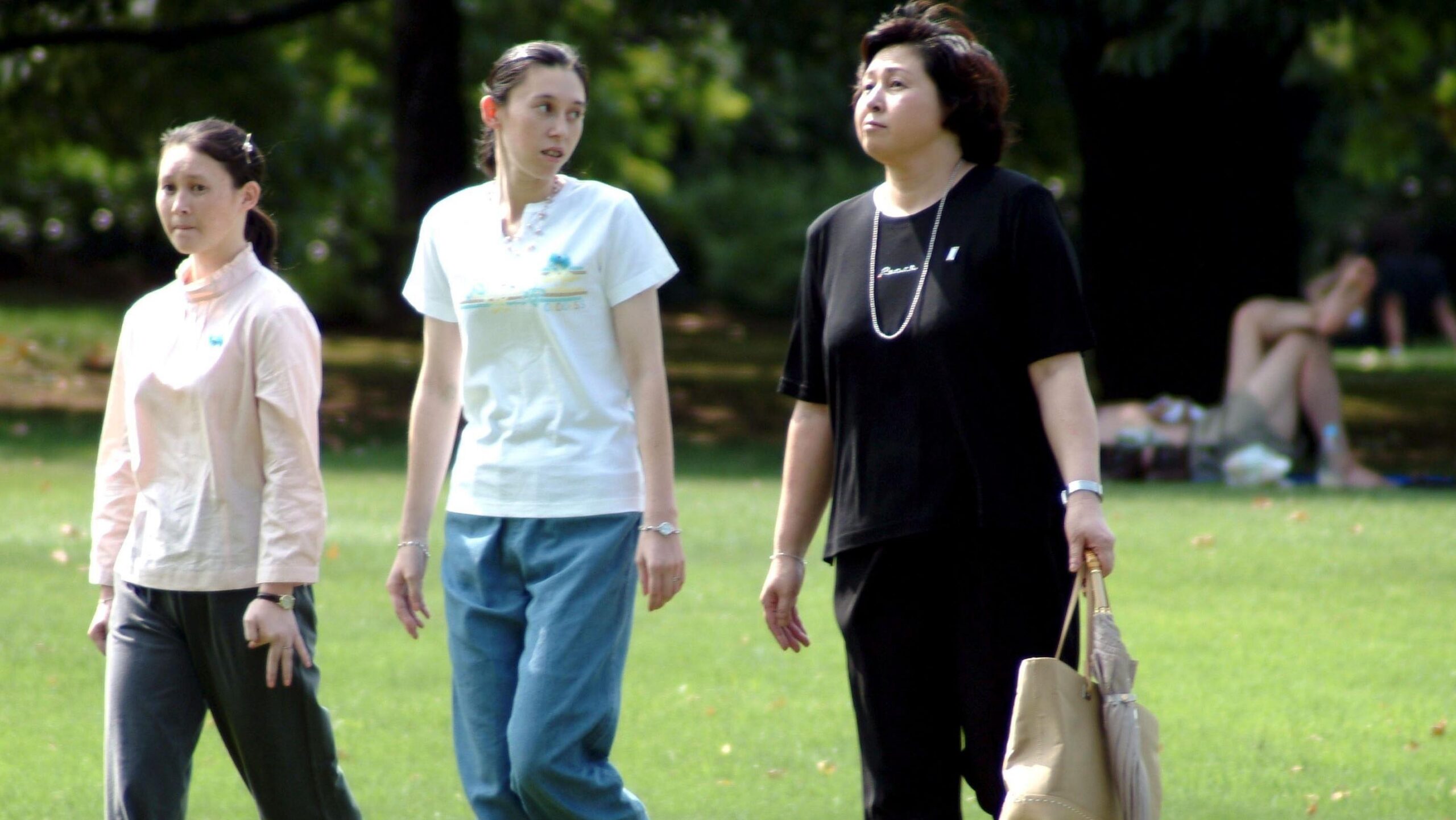 Hitomi Soga y sus dos hijas pasean por un parque. Soga lleva un bolso de mano color beige y un paraguas. 
