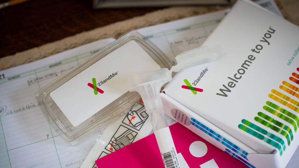 Sobre una mesa se extiende un kit de prueba de ADN casera, con el tubo para la recolección de saliva y el empaque bien visibles. La marca 23andMe es claramente visible, al igual que las palabras "Bienvenido a ti" y numerosas líneas de colores que forman la figura de un hisopo. 
