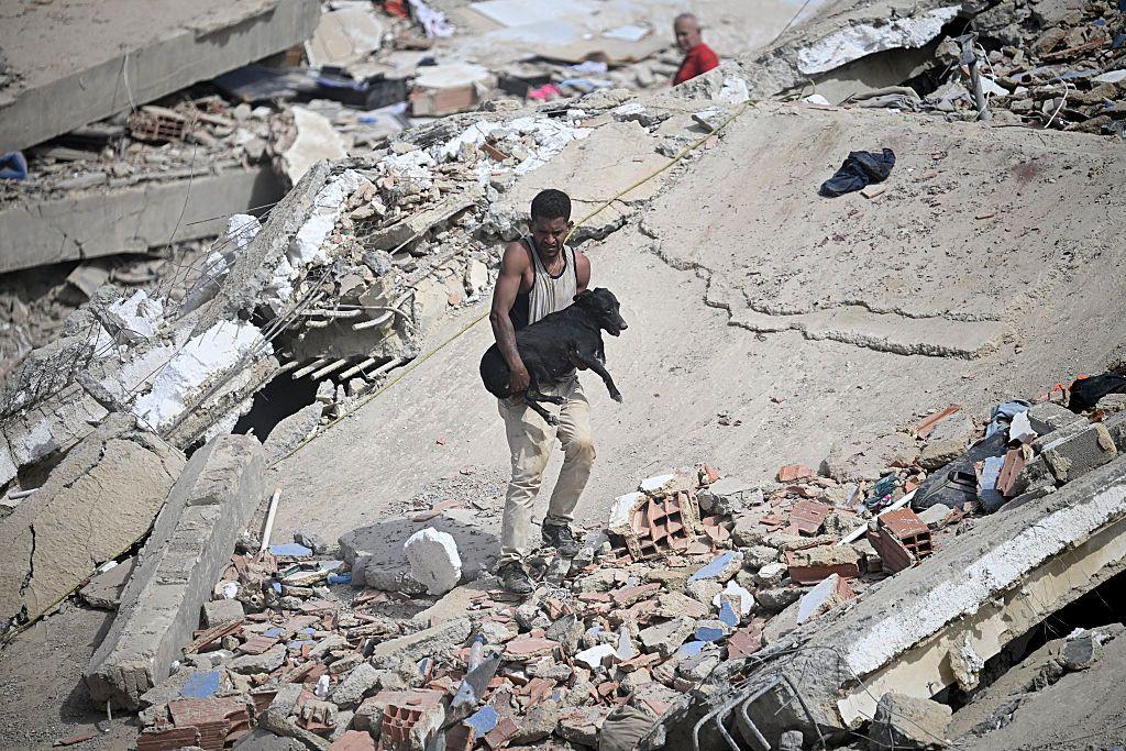 Un hombre lleva a un perro negro rescatado entre los escombros de un edificio derrumbado tras dos terremotos en Caraballeda, estado de La Guaira, a unos 40 km al noreste de Caracas, el 25 de junio de 2026.