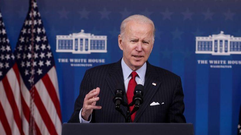 Joe Biden pronuncia un discurso. Viste un traje oscuro, camisa clara y corbata roja.