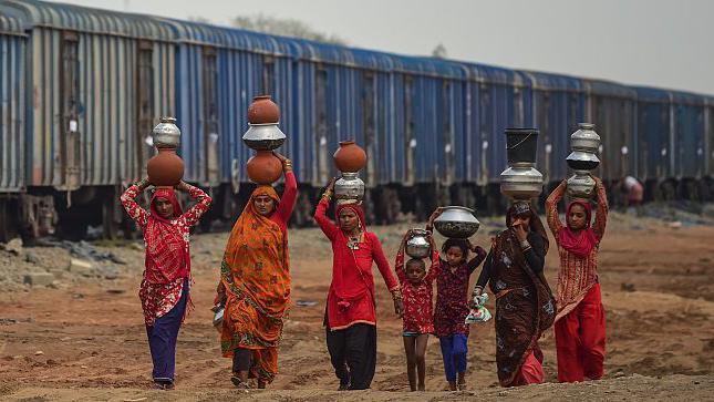 Mujeres cargando recipientes de agua en la cabeza en India.