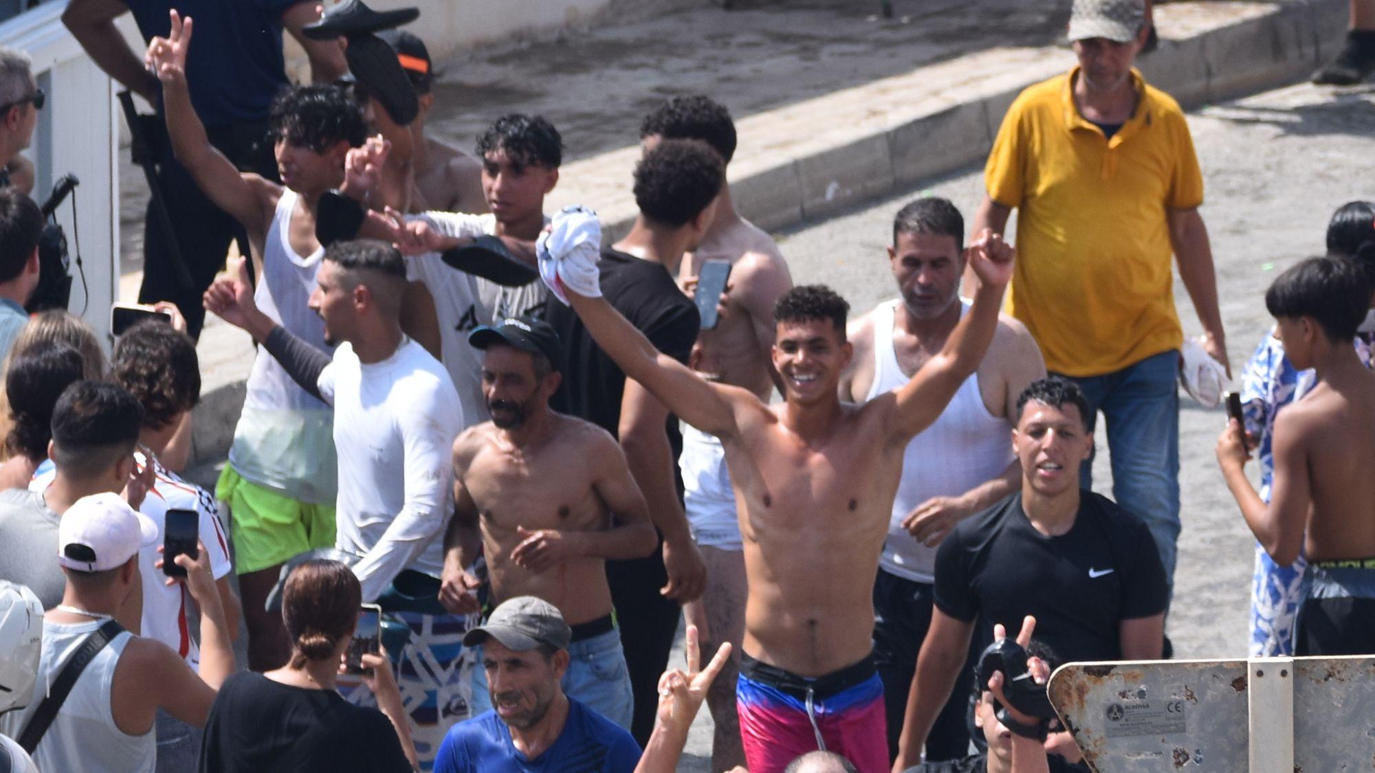 Migrantes pasan la frontera, algunos haciendo gestos de celebración.