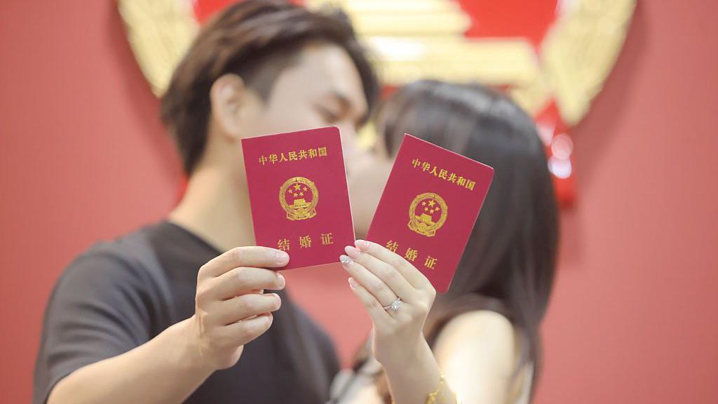 Una pareja de recién casados posa para una foto con sus certificados de matrimonio en Yangzhou, provincia de Jiangsu, China.