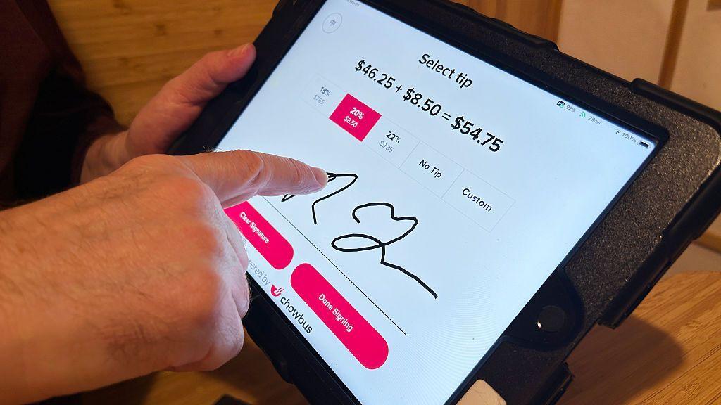 Persona selecciona una propina del 20% y firma en una tableta de pago digital en un restaurante.