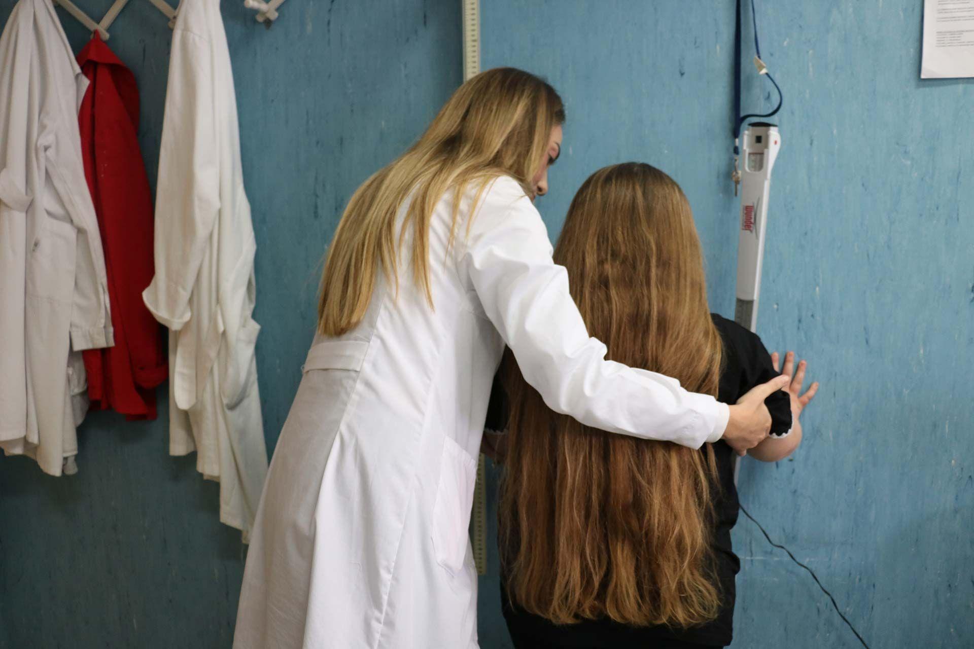 Una doctora, de espaldas a la cámara, ayuda a una niña a subirse a la báscula.