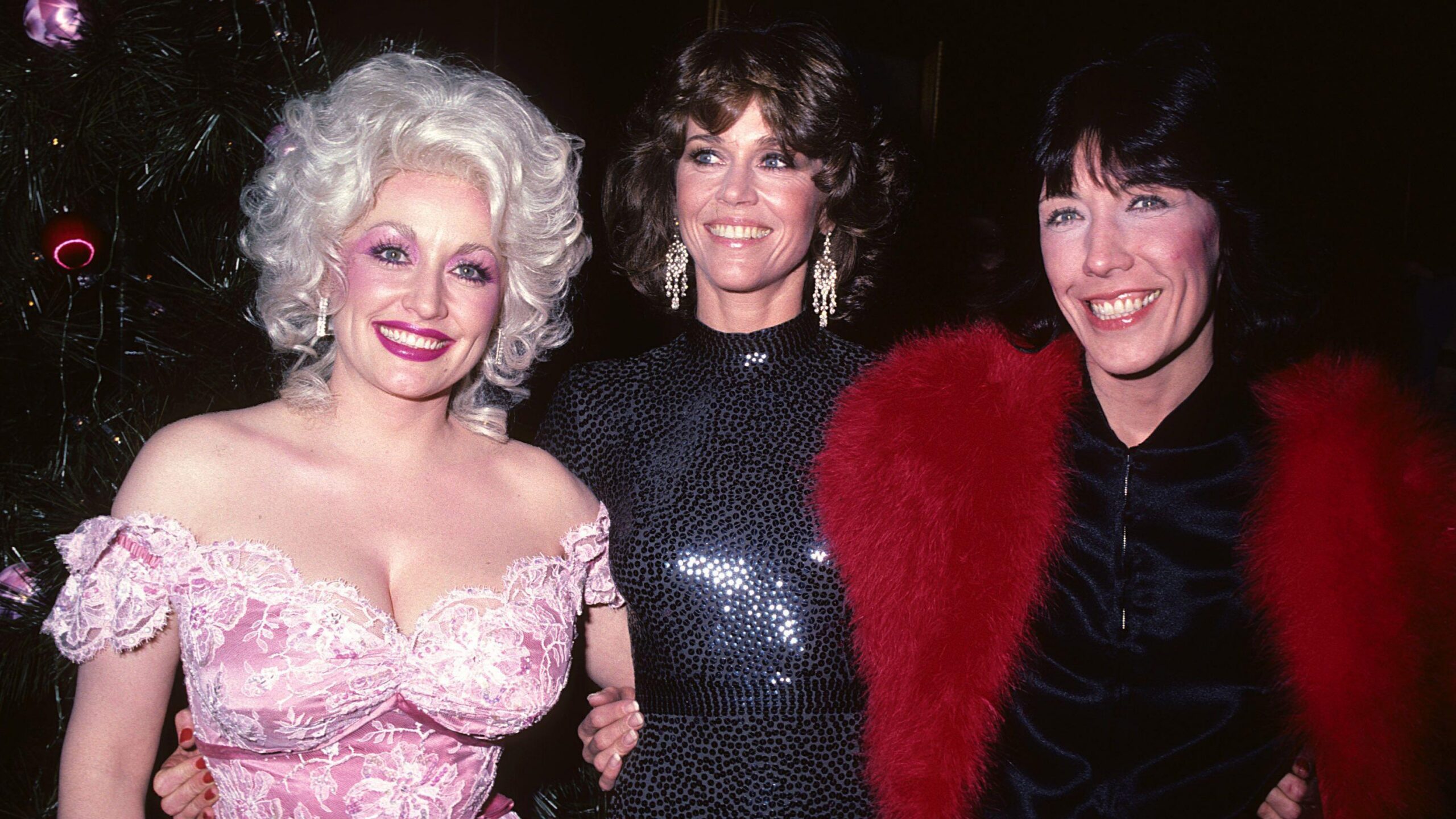 Dolly Parton, con un vestido rosa brillante sin tirantes, Jane Fonda con un vestido negro de lentejuelas de cuello alto y Lily Tomlin con un vestido negro y una estola de piel roja brillante.