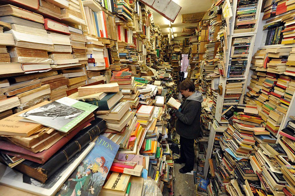 Joven parado en la mitad de una librería antigua rodeado de libros usados.