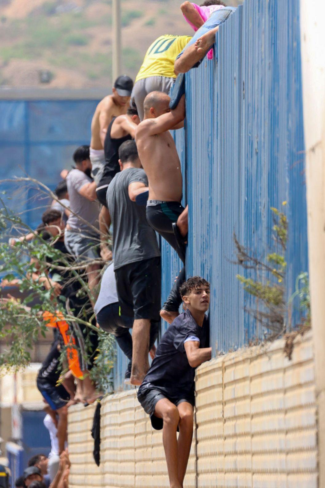 Migrantes trepan una valla en territorio español tras nadar desde Marruecos hasta Ceuta, un enclave español en el norte de África, el 30 de julio de 2026.