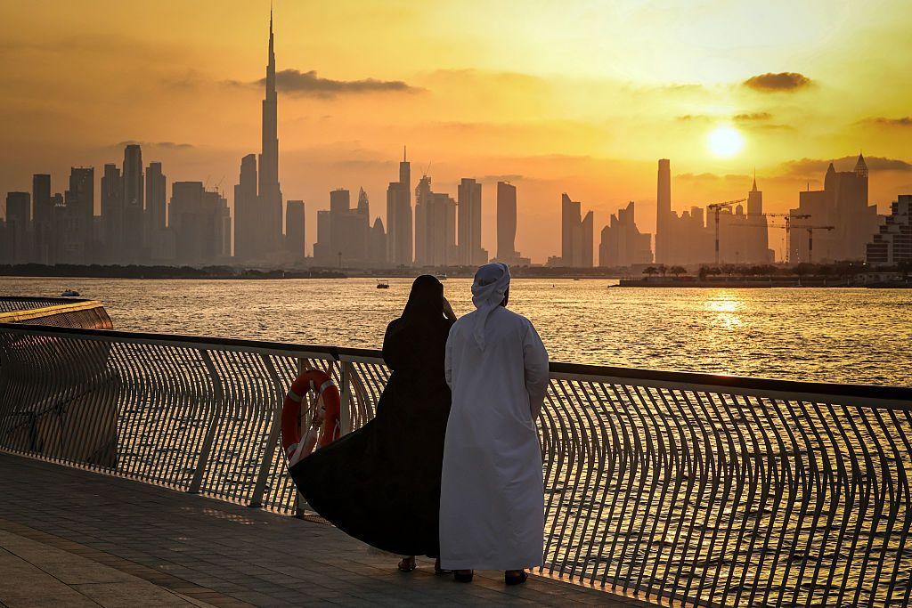 Una pareja mira los rascacielos de Dubái al atardecer desde un paseo marítimo.