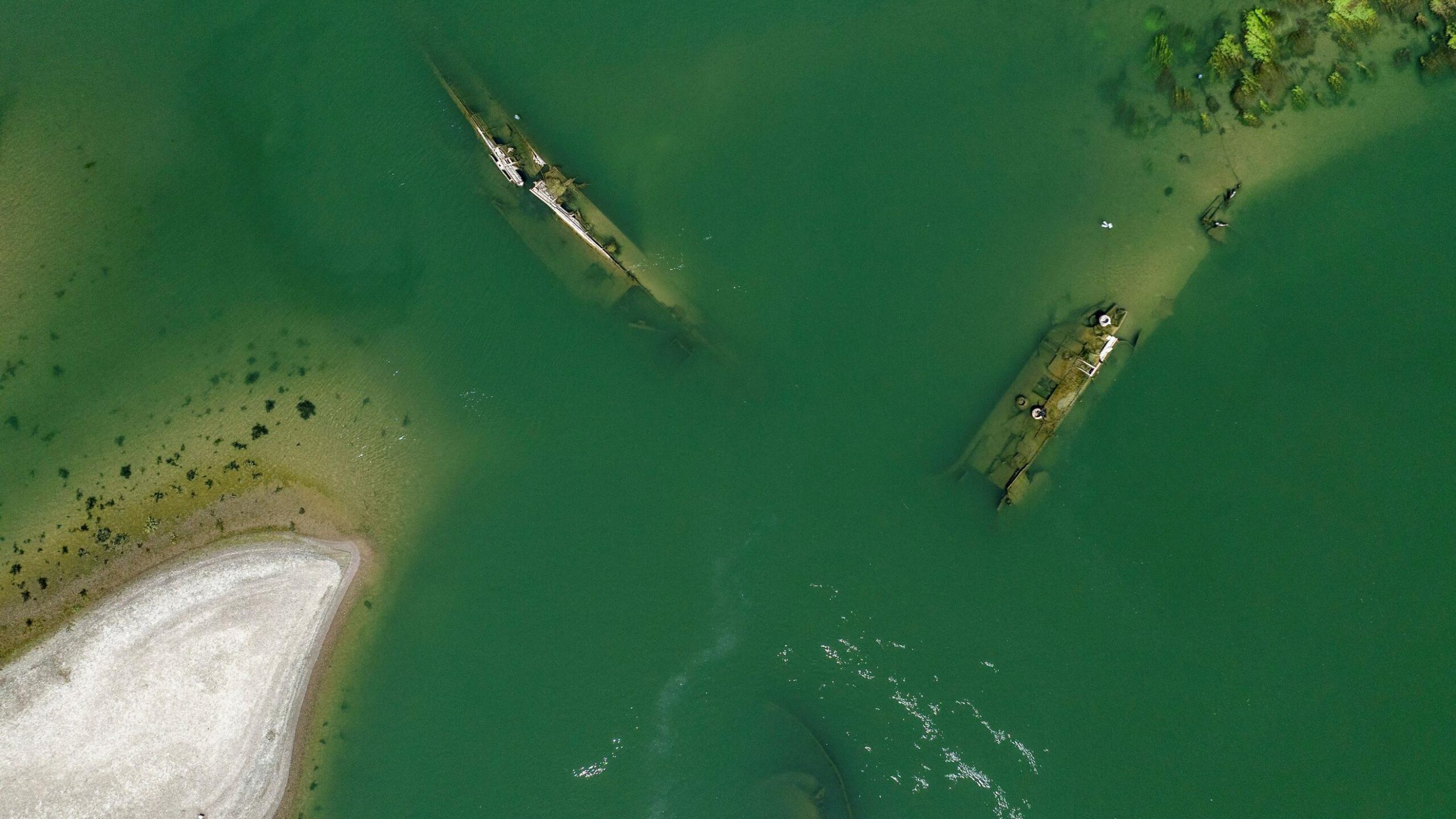 Las aguas verdes poco profundas revelan tres contornos de naufragios. Algunas partes de los barcos están expuestas mientras que otras aún están bajo el agua