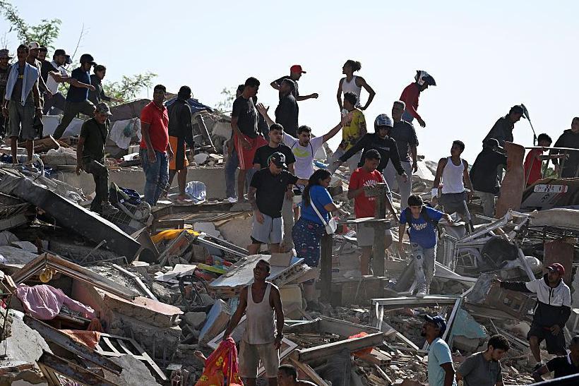 Un grupo de personas busca sobrevivientes mientras otros intentan rescatar sus pertenencias en un edificio derrumbado. 