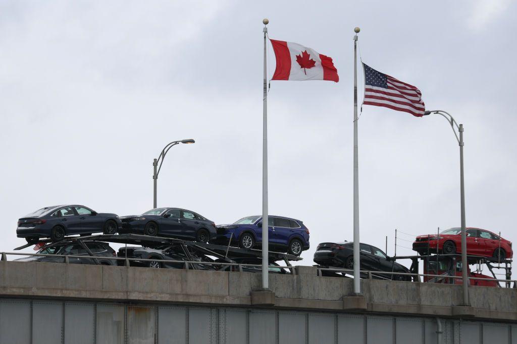 Un camión que transporta vehículos en la frontera en un puente y se ven las banderas de Canadá y de EE.UU.