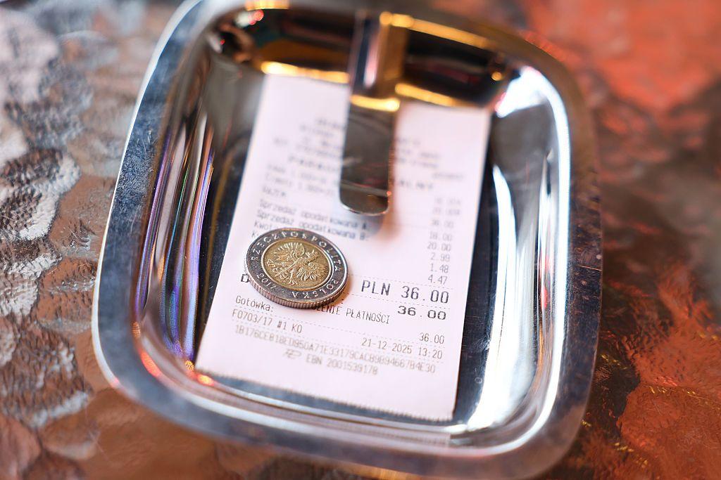 Bandeja metálica con un recibo y una moneda utilizada para dejar propina sobre una mesa.