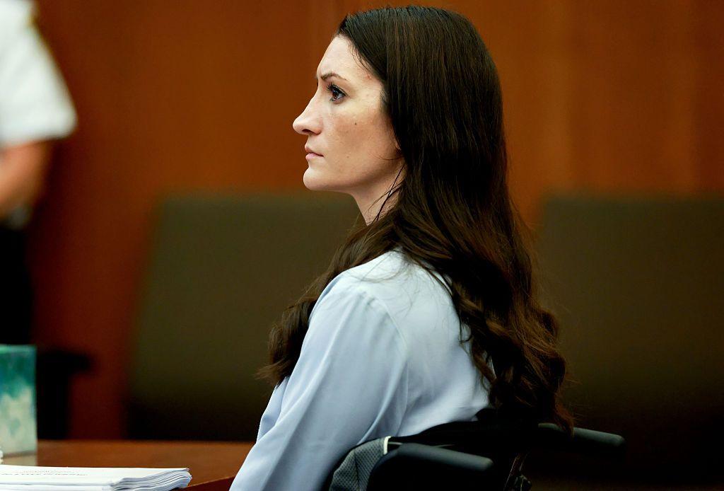 Clancy sentada en una silla de ruedas durante el juicio. Viste una blusa de color claro. Tiene piel blanca y una larga melena oscura. En la mesa frente a ella se distingue un taco de papeles. 