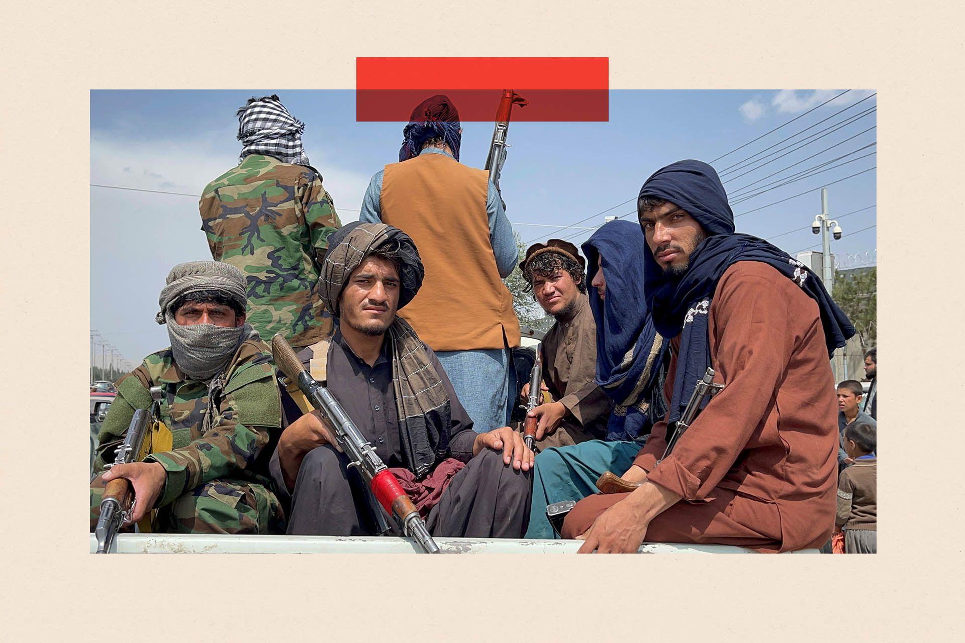 Combatientes talibanes vestidos con ropas tradicionales y armados van sentados en la parte trasera de un vehículo descubierto. 