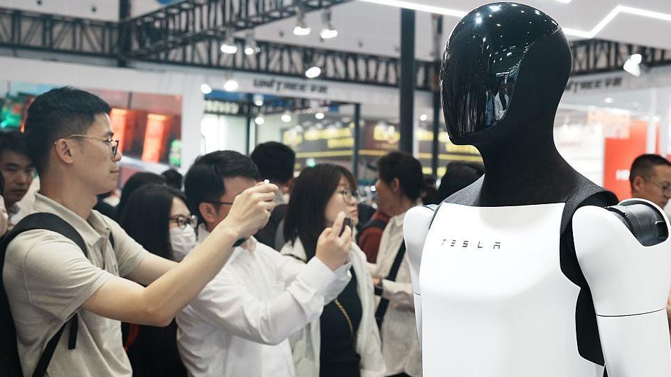 En una exposición en China, la gente toma fotografías del prototipo humanoide Optimus de Tesla.