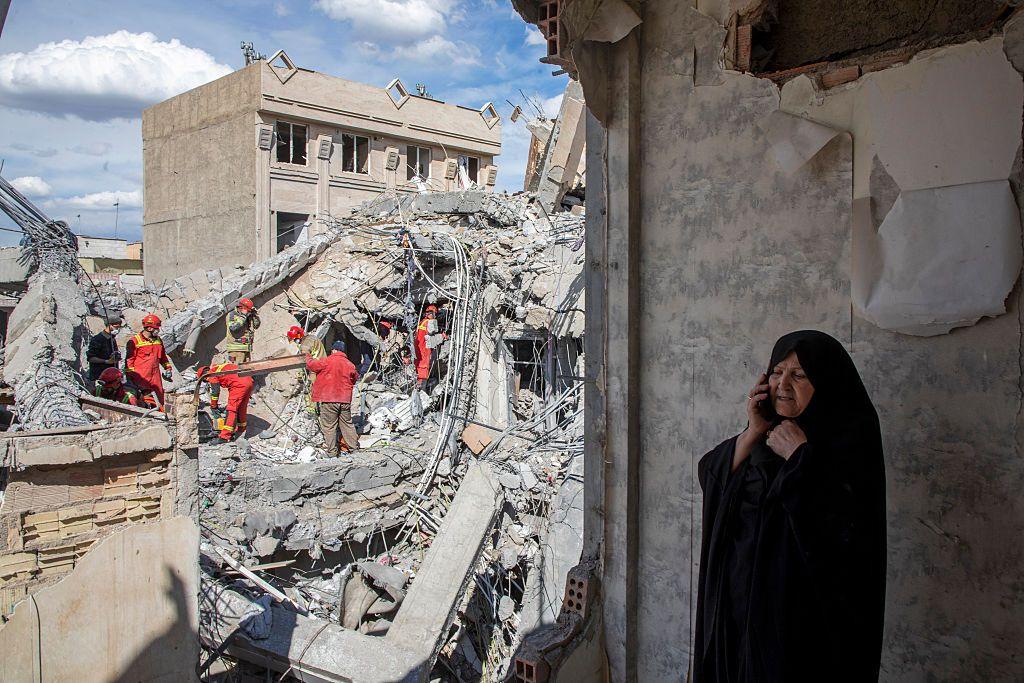 Una mujer habla por teléfono móvil mientras los equipos de emergencia remueven los escombros de un edificio residencial que fue alcanzado por un ataque aéreo en la madrugada del 27 de marzo de 2026 en Teherán.
