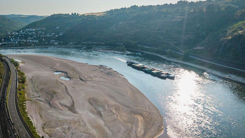 Vista aérea de un buque de carga pasando junto a un enorme banco de arena en el río Rin.
