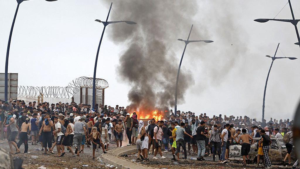 Cientos de personas que cruzaron la frontera se congregan alrededor de una estructura que fue incendiada en el enclave español de Ceuta, en el norte de África.
