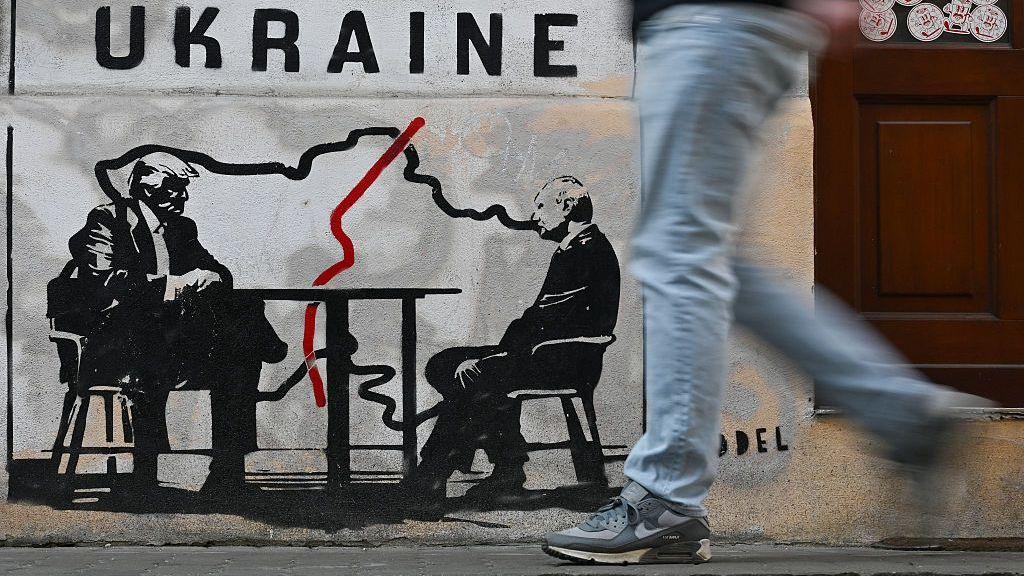 Un hombre pasa frente a un mural del artista callejero noruego Toddel que representa un mapa de Ucrania y al presidente de EE.UU., Donald Trump (izq.), junto al presidente de Rusia, Vladimir Putin, en Cracovia, el 6 de marzo de 2026.