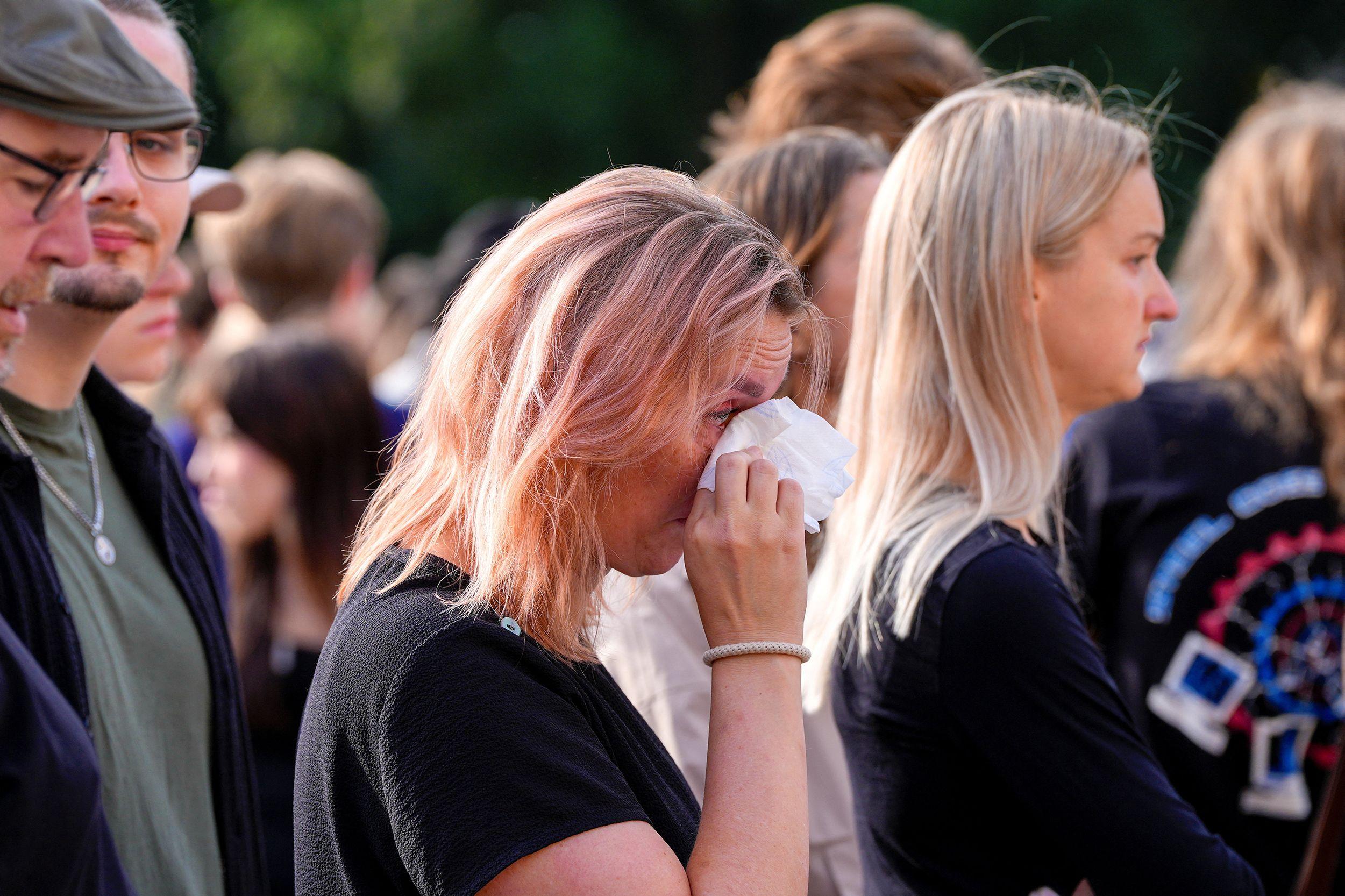 Asistente en una concentración al aire libre se seca el rostro con un pañuelo mientras permanece entre otras personas reunidas para un homenaje público.