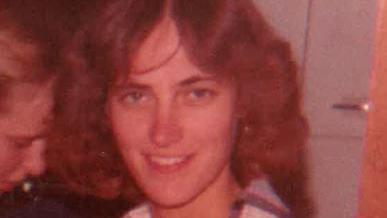 Karen Schepers sonríe a la cámara, con su cabello castaño ondulado partido por la mitad al estilo típico de principios de los años 80. 