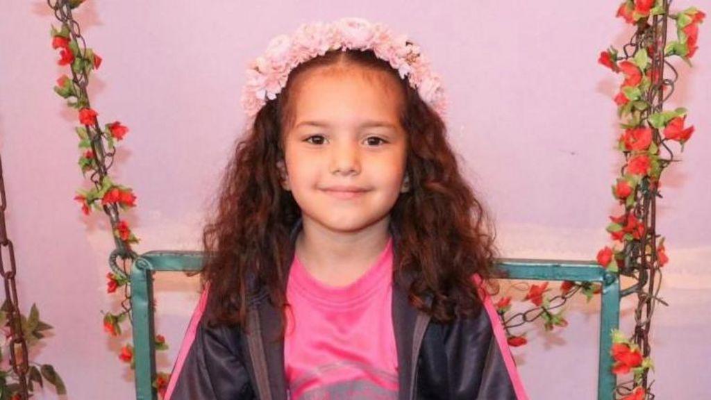 Hind Rajab en primer plano, sonriente, con una diadema de flores en el pelo y adornos florales detrás