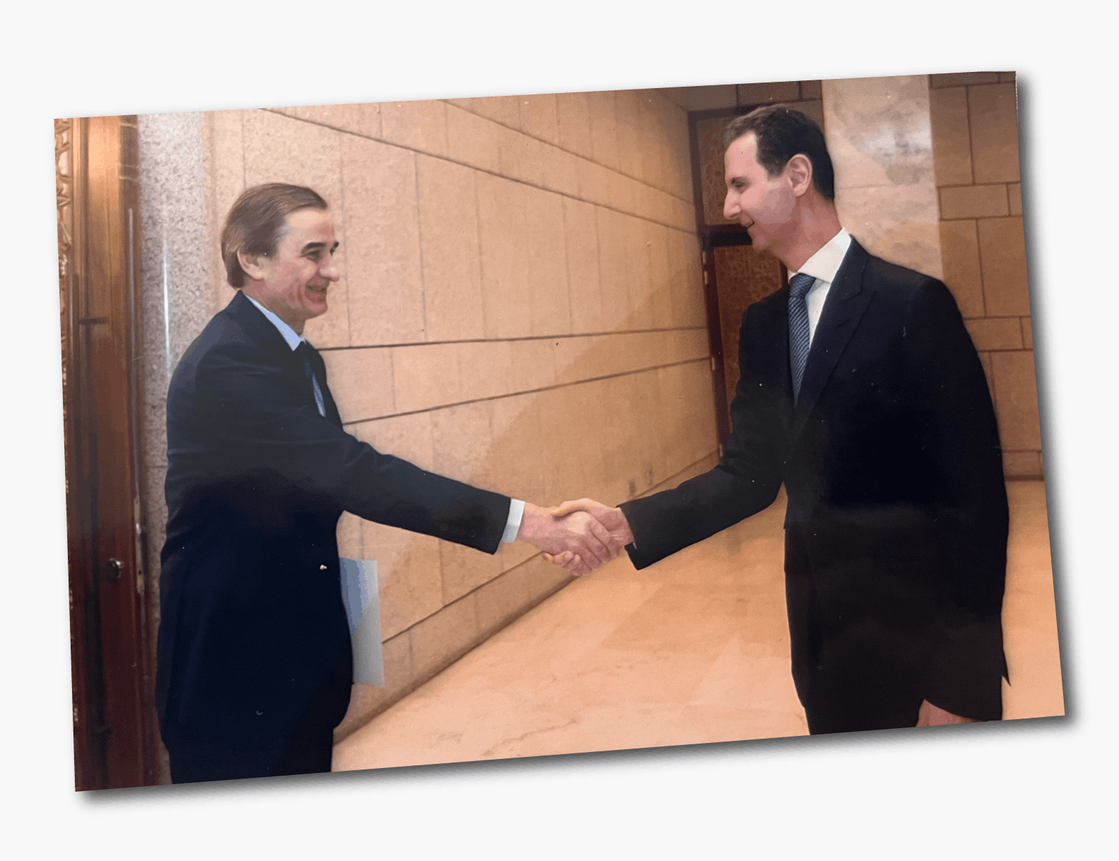 Una foto de Hussam Luka estrechando la mano de Assad; ambos visten trajes oscuros y sonríen. 