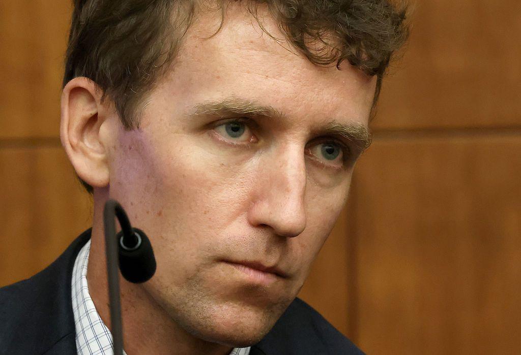 Patrick Clancy, en primer plano, durante su declaración en el juicio. Tiene piel blanca y pelo corto castaño. Viste una americana oscura sobre una camisa blanca con finas rayas entrecruzadas. 