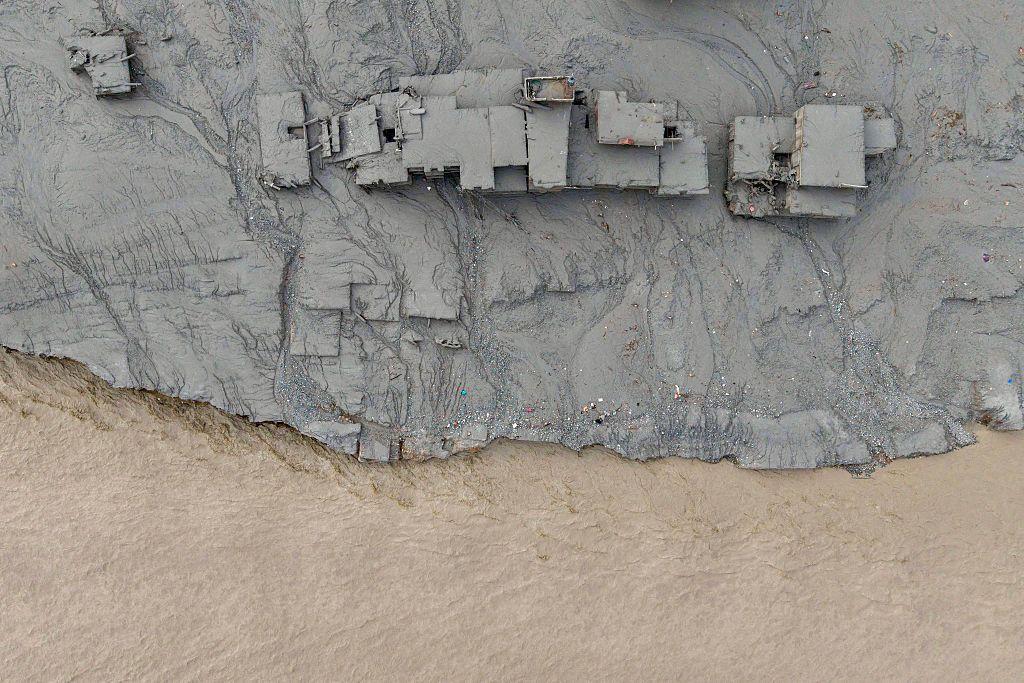 Un río marrón pasa al lado de una serie de construcciones cubiertas de barro debido a una avalancha reciente. La foto es tomada desde arriba. 