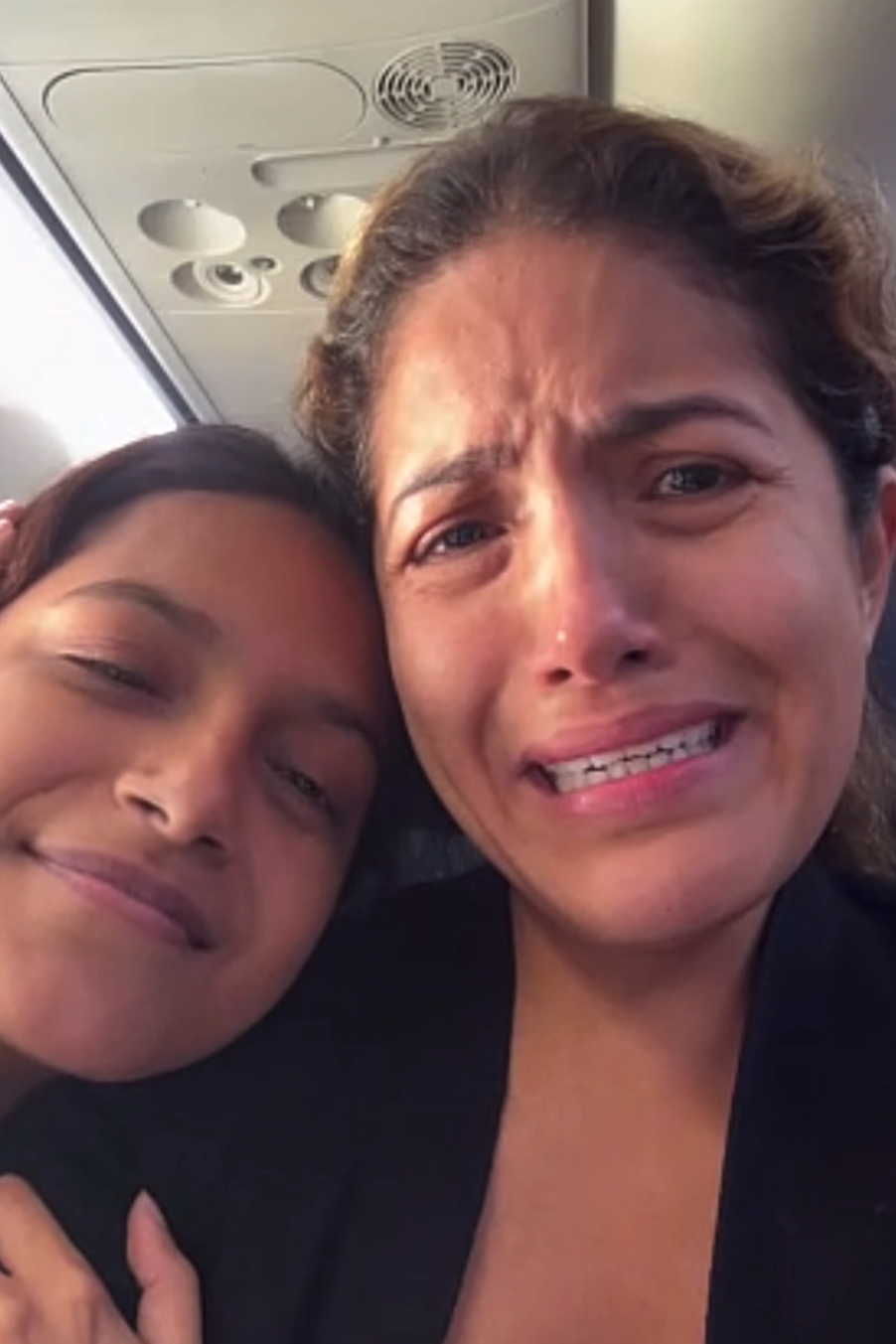 Una mujer y su hija dentro de un avión. La joven sonríe y su madre llora.