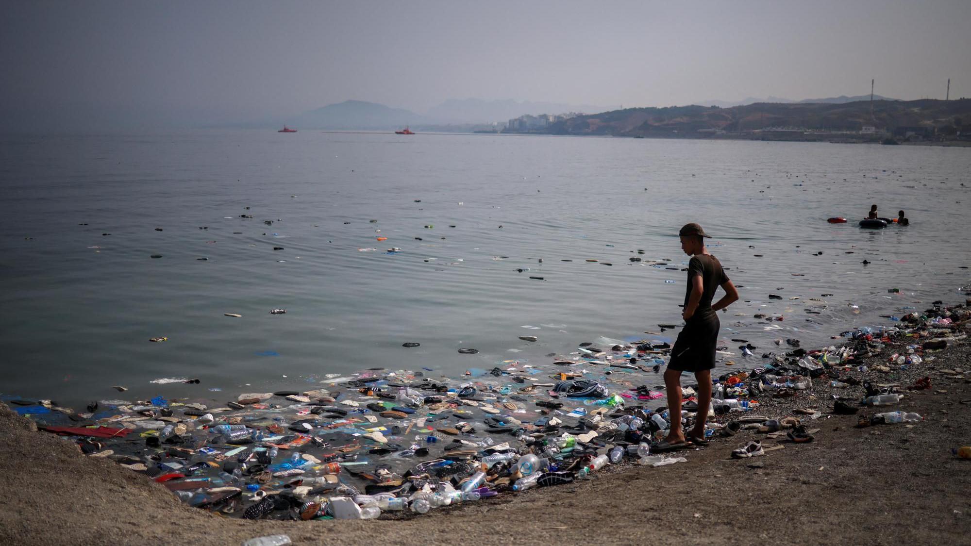 Un migrante observa las zapatillas deportivas en el agua tras las travesías masivas de migrantes a pie y por mar desde Marruecos hacia territorio español.
