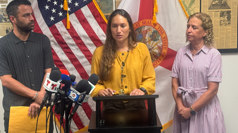 Claudia Rodríguez, en el centro, vestida con una camisa amarilla, habla a los medios durante una rueda de prensa. A su derecha la acompaña la congresista Debbie Wasserman Schultz. 