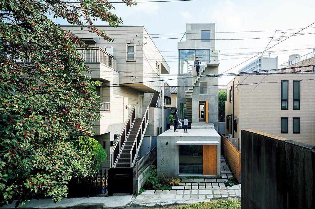 Vivienda urbana de hormigón visto con terrazas escalonadas y escalera exterior, rodeada de edificios residenciales.