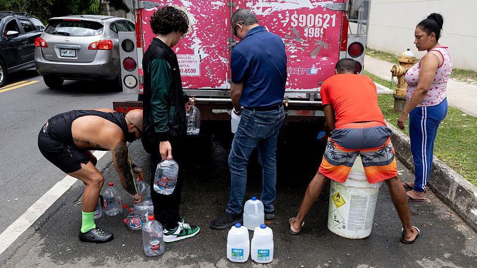 Un grupo de personas llenando recipientes de agua en un camión.