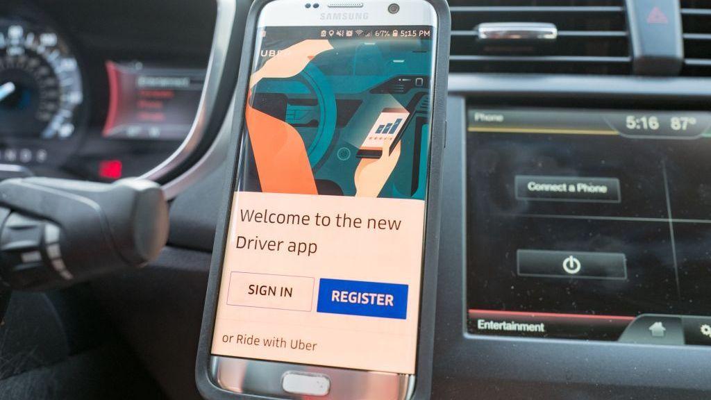 Primer plano de un teléfono inteligente que muestra la aplicación para conductores de Uber, colocado en un soporte magnético para salpicadero en el interior de un vehículo Uber