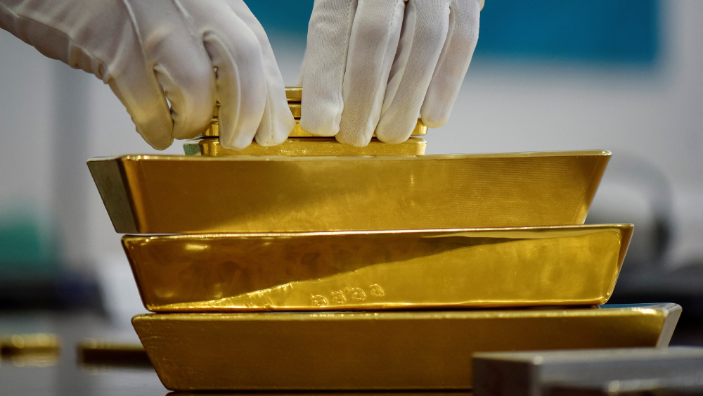 Dos manos en guantes blancos manipulan varios lingotes de oro