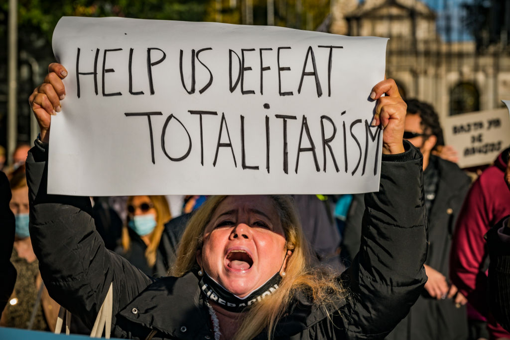 Mujer sosteniendo pancarta que dice: "Ayúdanos a vencer el totalitarismo".