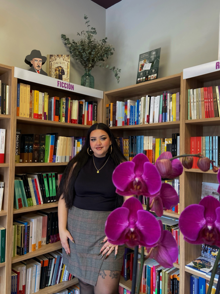 Rosa Ramírez Mazaheri de pie contra una estantería llenas de libros en la que se lee 