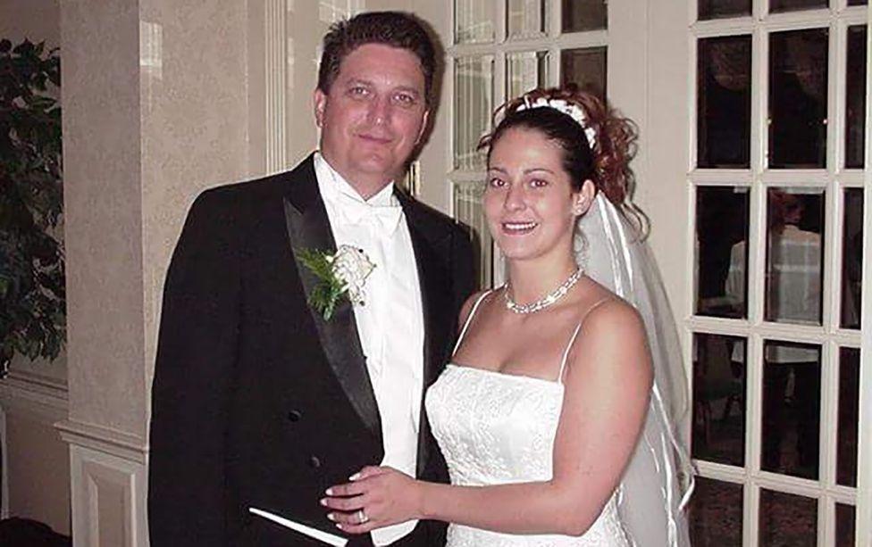 A la izquierda, John lleva su traje de boda con una flor en la solapa. A la derecha, Sylvia luce un vestido de novia y una tiara. Ambos sonríen a la cámara.