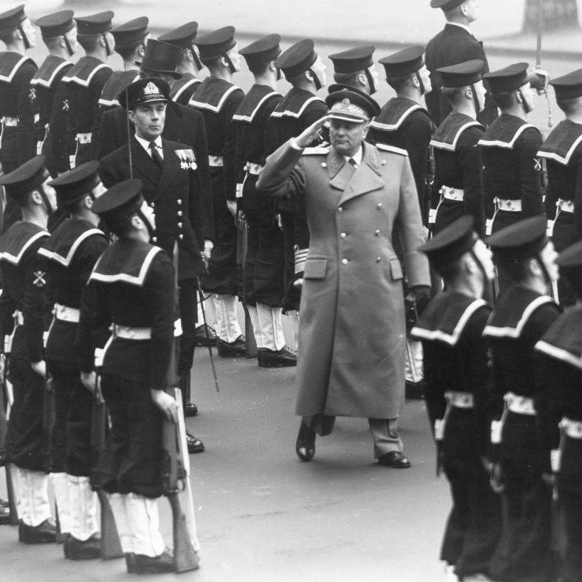 Foto en blanco y negro de Tito haciendo un saludo marcial y rodeado de marinos ingleses en posición de firmes.