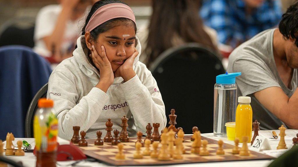 Bodhana Sivanandan, con una sudadera gris con capucha, apoya la cara en las manos mientras mira un tablero de ajedrez frente a ella.