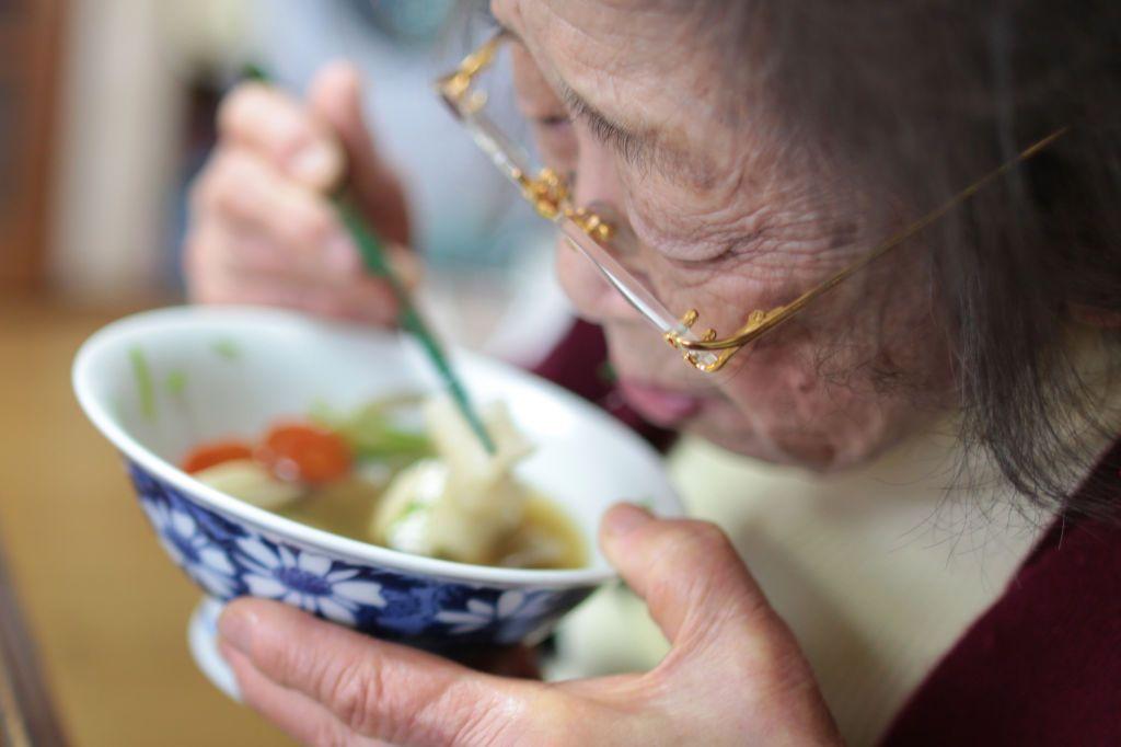 Primer plano de una anciana japonesa comiendo sopa de fideos. 