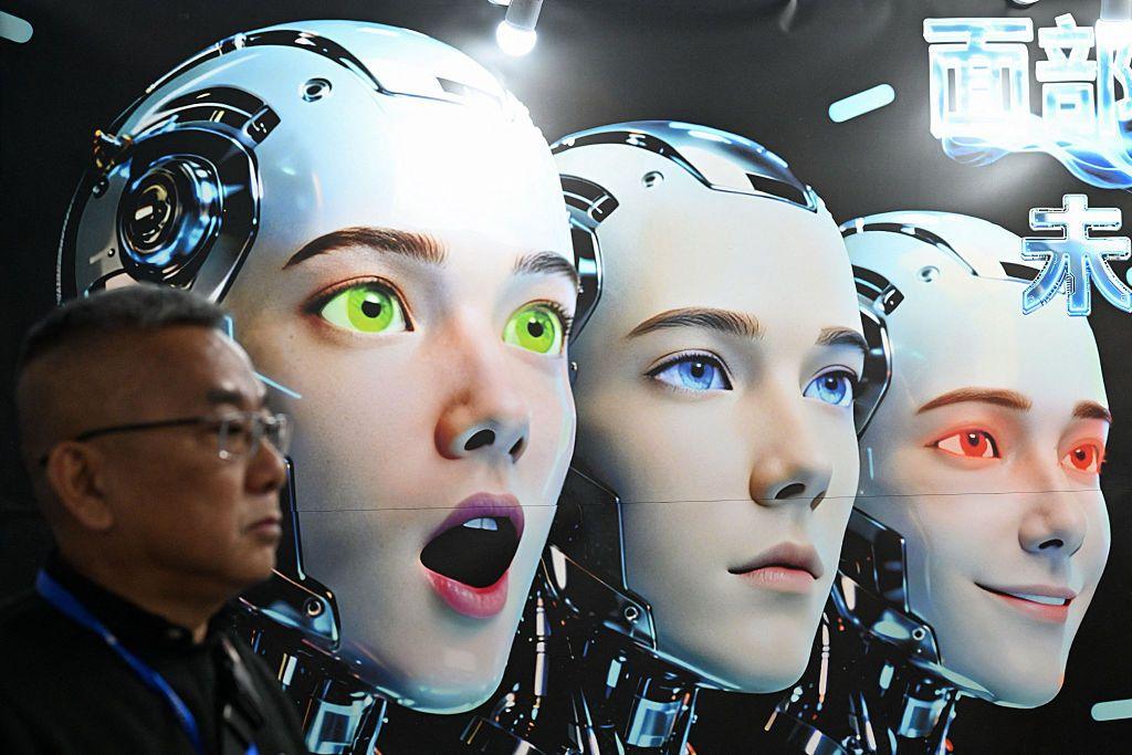 Un hombre parado junto a un cartel en el que se muestran robots que imitan expresiones humanas, de la empresa Shenzhen Xiaoquan Technology, durante la Exposición Internacional de Aplicaciones de Inteligencia Artificial e Innovación en Robótica celebrada en Pekín.