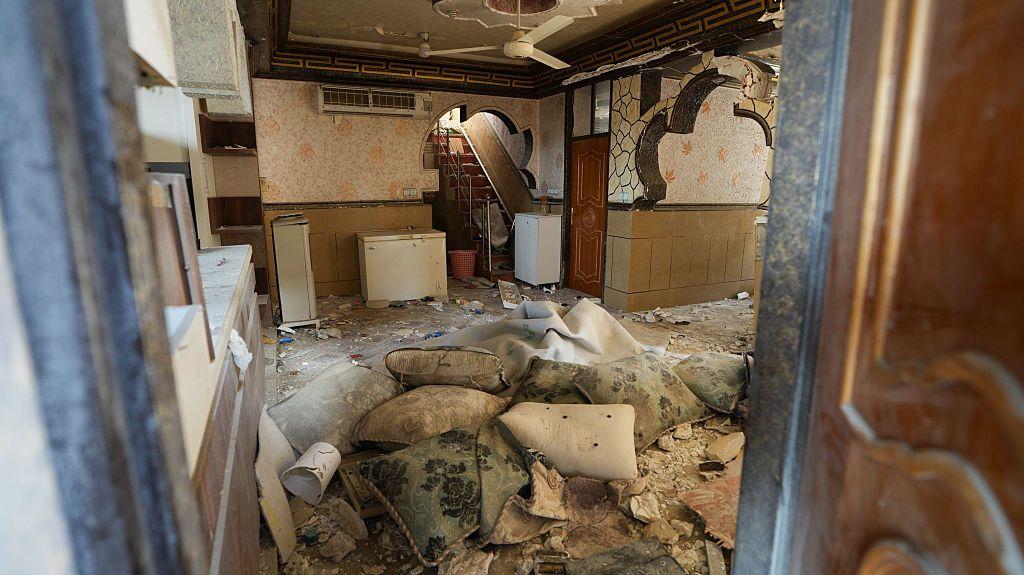 Interior de un edificio atacado en Kuhestak, Irán. Se ven paredes dañadas y cojines y almohadones amontonados en el centro de la estancia. 
