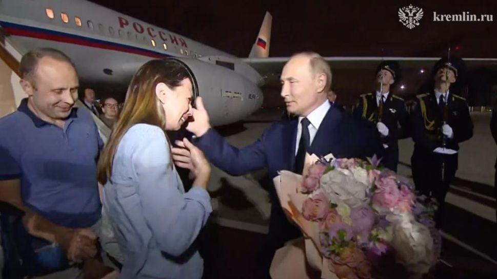 Vladimir Putin, con un ramo de flores en la mano, recibe a una pareja que desciende de un avión. La mujer parece feliz.