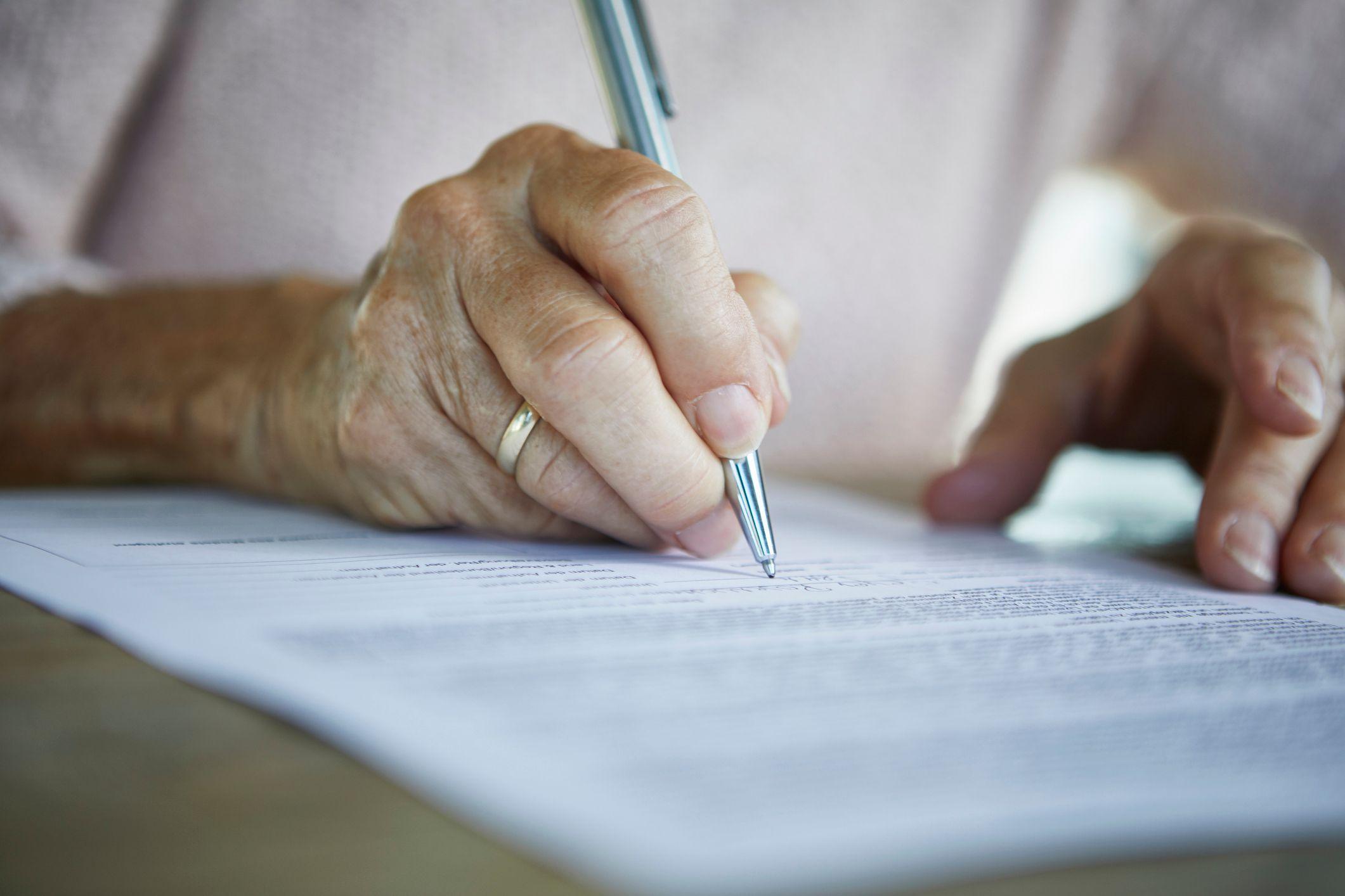 La mano de una mujer mayor firmando un documento legal.