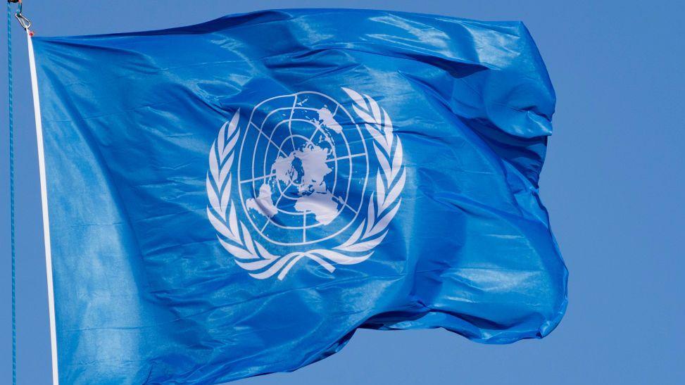 La bandera de las Naciones Unidas ondea al viento en un mástil. El emblema, de color blanco, representa el mapamundi en proyección azimutal equidistante, rodeado por dos ramas de olivo. Foto de archivo