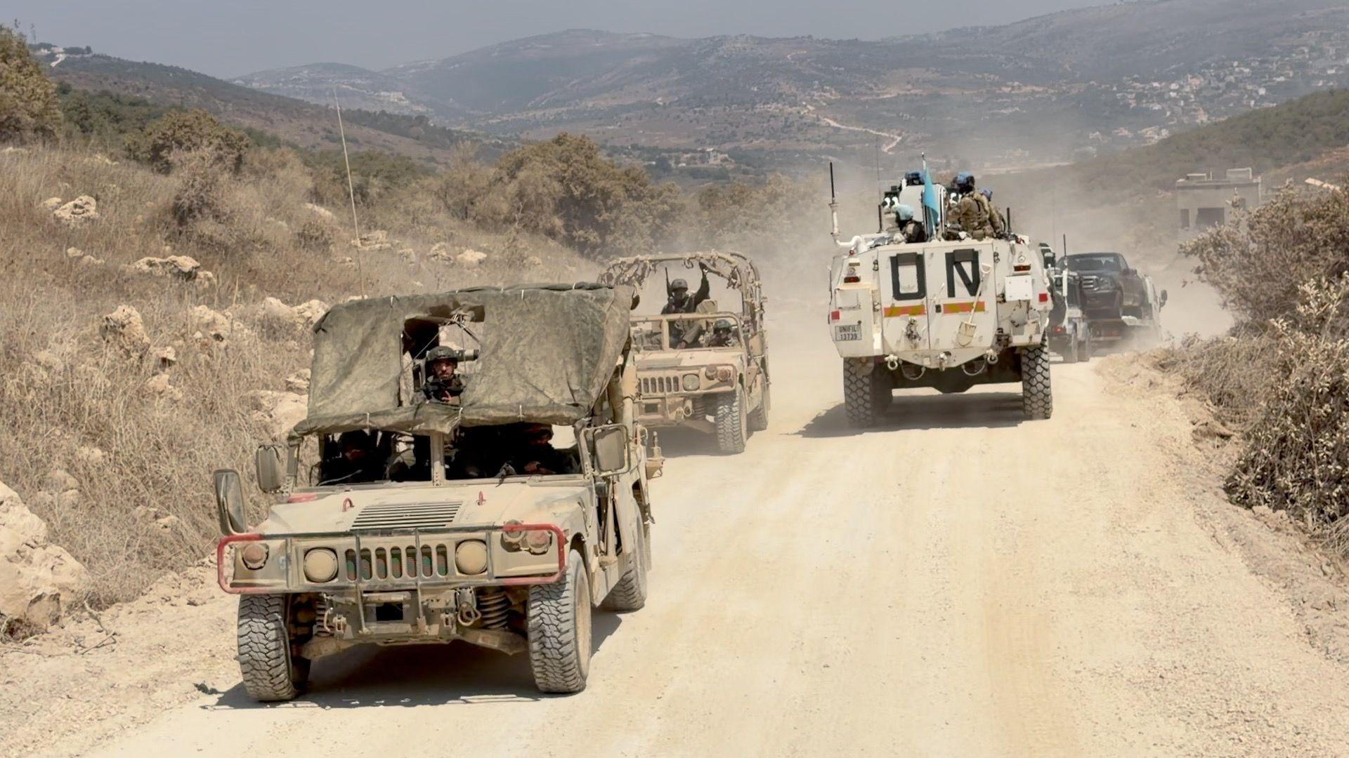Dos vehículos militares israelíes adelantan a un convoy de la UNIFIL en una carretera que discurre junto al muro que separa Líbano e Israel.