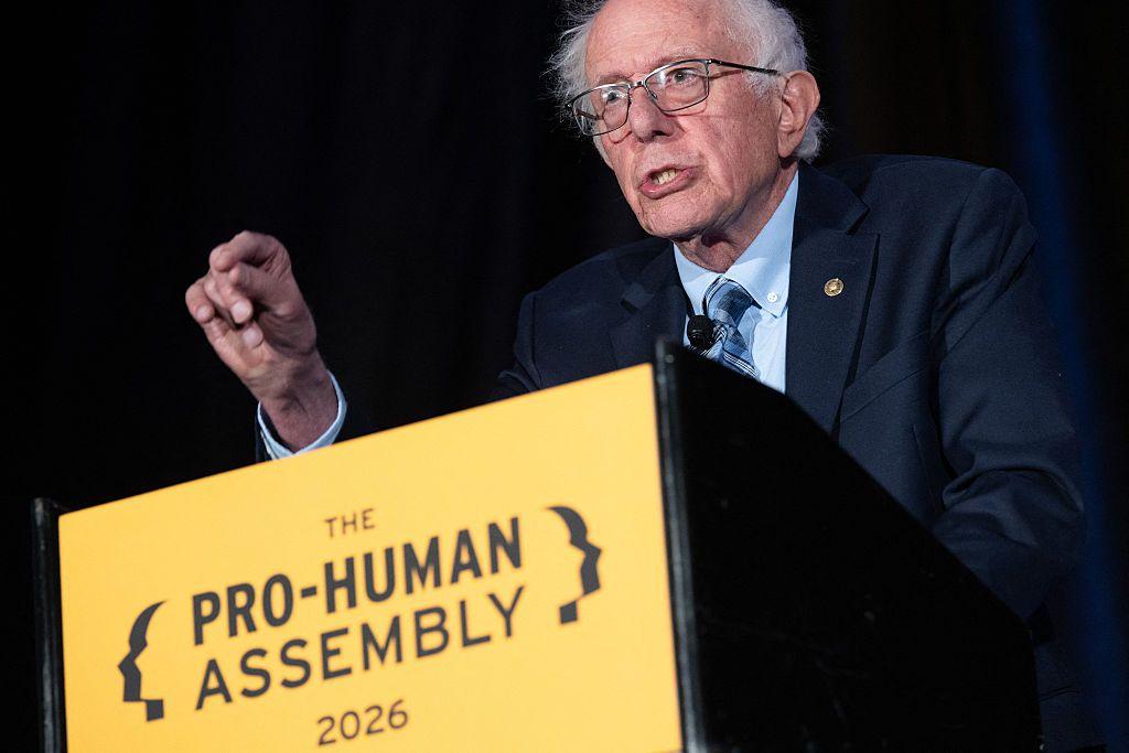 El senador Bernie Sanders habla en un estrado amarillo. El viste un traje de color azul. 